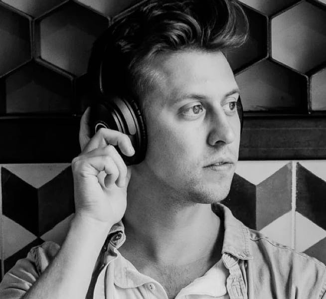A young Caucasian man wearing headphones, looking to the right, with a honeycomb patterned backdrop