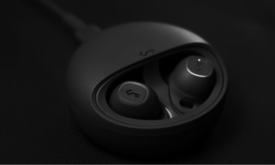 Wireless earphones inside a black case, connected to a charging cable