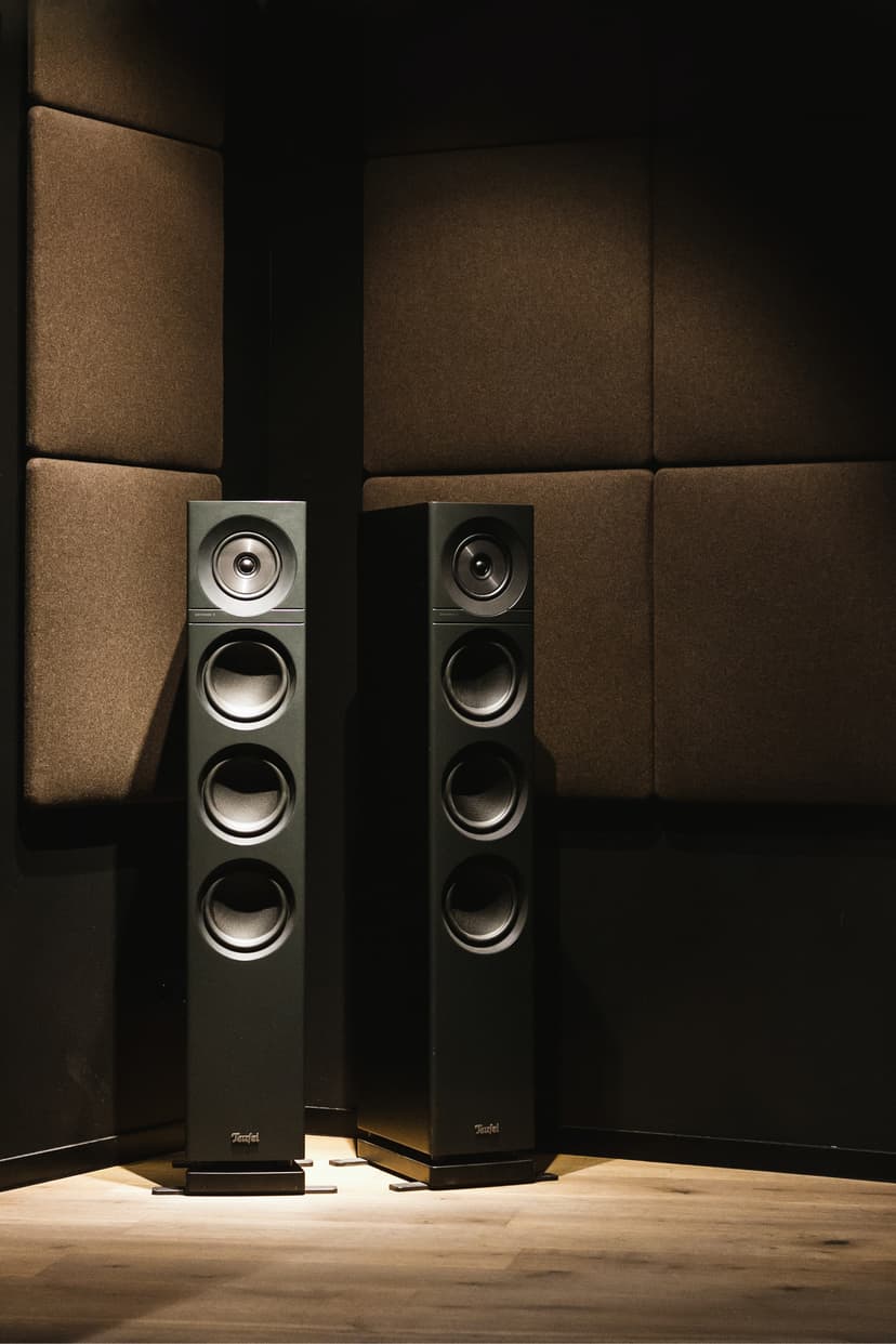 Two slim tall subwoofers in the corner of a padded studio